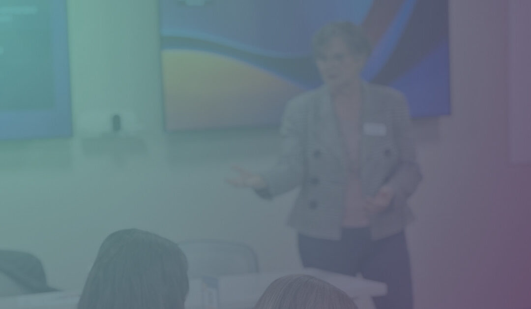 A blurred image shows a person in a gray blazer conducting a presentation in front of an audience. Attendees are seated, facing the speaker.