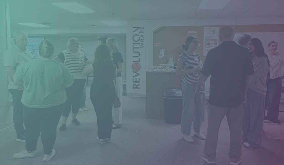 A group of people casually chatting in an office space with a "Revolution Wraps" sign.